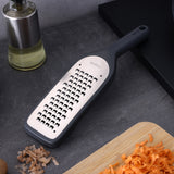 The Zyliss Coarse Grater, featuring a metal and plastic build with an ultra-sharp blade and black handle, sits on a gray countertop beside a cutting board with shredded carrots—an essential meal prep tool.