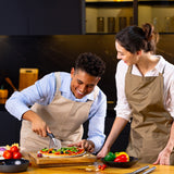In a modern kitchen, two people in aprons smile while one slices a fresh pizza using the Zyliss Pizza & Pastry Cutter with an ergonomic handle. Colorful vegetables sit on the table, and they look like theyre enjoying cooking together.