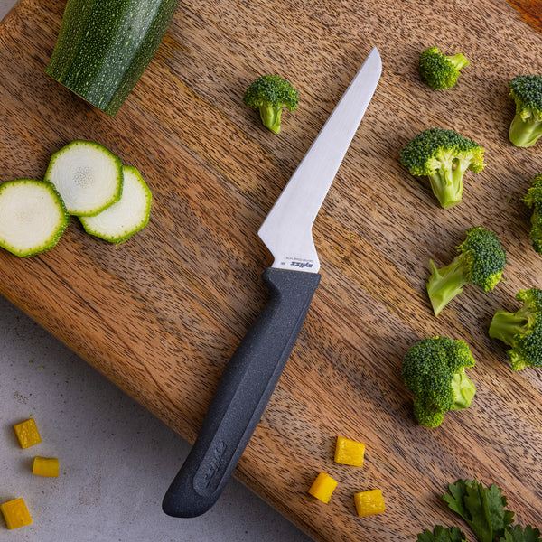 A Zyliss Offset Knife 10cm / 4 with a black eco-friendly handle sits on a wooden cutting board, surrounded by chopped zucchini, broccoli florets, and diced yellow bell pepper.